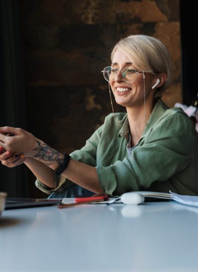 Iloinen henkilö istuu tietokoneella korvanapit korvissa